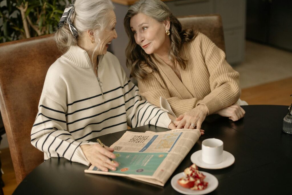 Two elderly women enjoying a cozy winter morning, sharing a heartfelt conversation over coffee and a newspaper.