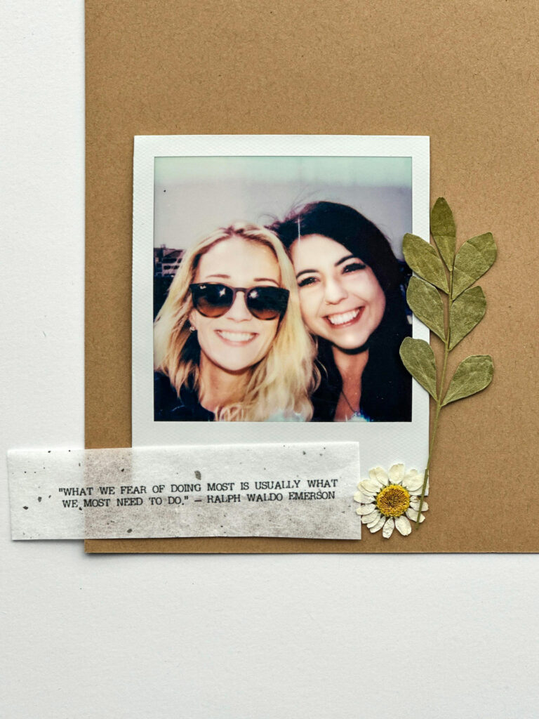 A Polaroid photo of two smiling women on a vision board, decorated with dried flowers and an inspiring quote.